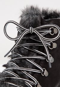 Botte d'hiver noire avec bordure en fausse fourrure grise, œillets métalliques et lacets rayés noir et blanc noués en nœud.