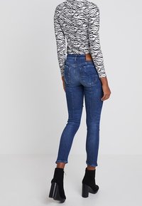 Jeans ajustados en denim azul oscuro con una textura suave, que presentan una cintura de altura media y un sutil bordado en los bolsillos traseros, combinados con botas de tobillo negras.