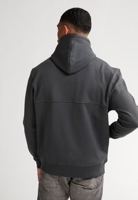 Sudadera con capucha gris de tela texturizada, que cuenta con un bolsillo canguro, puños acanalados y una costura en la parte superior de la espalda.