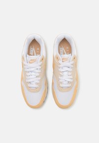 Ténis Nike Air com um esquema de cores laranja claro e branco, apresentando um upper em malha, língua almofadada e detalhes texturizados nos lados.