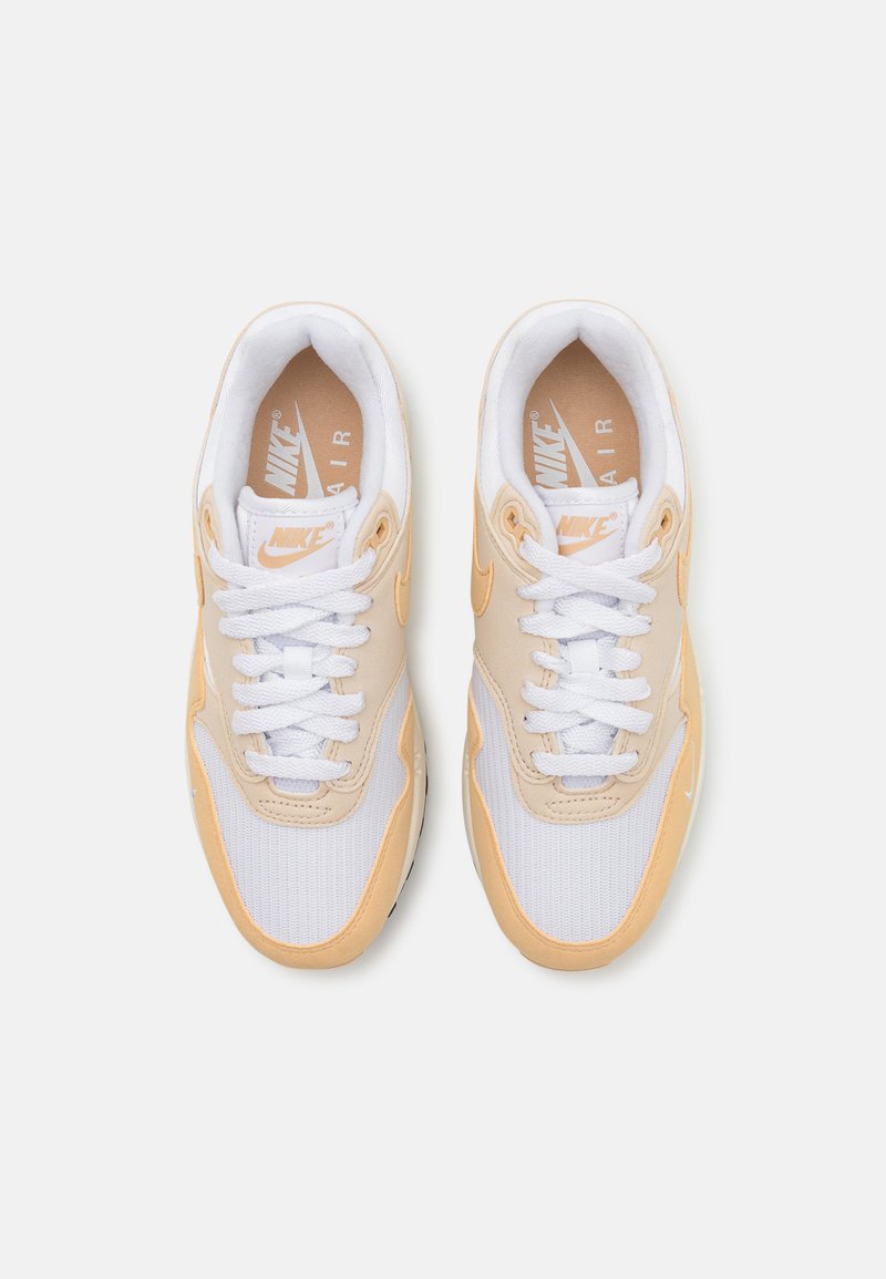 Zapatillas Nike Air con una combinación de colores naranja claro y blanco, que cuentan con una parte superior de malla, lengüeta acolchada y detalles texturizados en los lados.