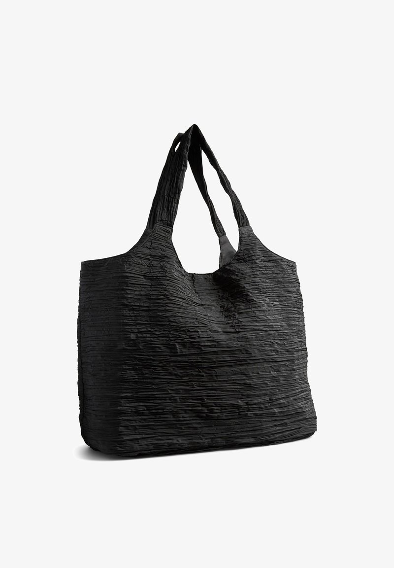 Sac fourre-tout texturé noir avec de larges doubles poignées, structure souple et surface du tissu légèrement froissée.