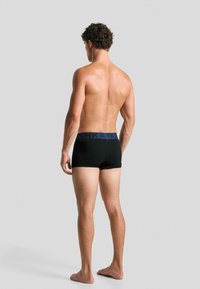 Boxeri negri cu o bandă elastică albastră, având o textură netedă și un design ajustat, prezentați din spate cu picioare goale.