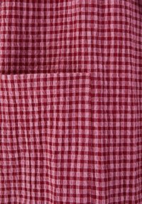Tissu à carreaux rouge et rose avec une petite poche carrée cousue dessus.