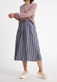 Jupe midi à rayures bleu et blanc avec une taille à cordon, associée à un pull rose clair et des baskets beiges. Texture mate, design décontracté.