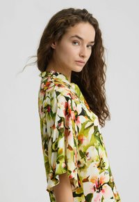 Gėlių kimono su žaliais, rožiniais ir geltonais gėlių raštais. Lengvas, šilkinis audinys, laisvas pavyzdys su raukšlėtomis rankovėmis.