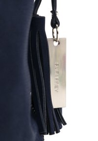 Tamsus maišas su lygiu audiniu, puošiamas dekoratyviniais kutais ir metaliniu ženkliuku su įspaudu "SURI FREY."