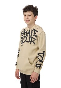 Felpa beige con tasca frontale. Caratterizzata da un grande testo nero "SKATE TOUR" e testo più piccolo sulle maniche. Tessuto morbido con una vestibilità classica.