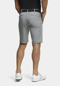 Shorts gris avec une texture lisse, design ajusté et deux poches arrière. Associés à des chaussures de golf blanches et une ceinture tissée noire.