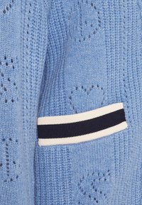Tissu tricoté bleu clair avec des motifs en forme de cœur et un détail de rayure horizontale blanche et bleu marine sur un poignet ou une manche.