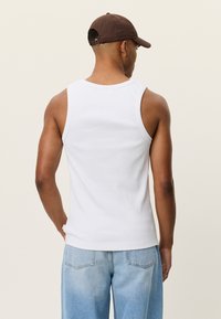 Débardeur blanc côtelé à coupe ajustée, avec des bretelles larges et un col rond, accompagné d'un jean en denim bleu clair.