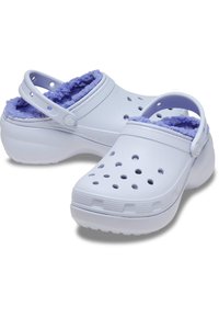 Sabots blancs avec une doublure en fourrure violette, dotés de trous de ventilation, d'une sangle au talon et d'une semelle texturée pour une meilleure adhérence. Matériau en plastique durable.