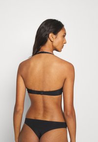 Ensemble de bikini noir avec un haut à nouer et un bas à couverture minimale. Dispose d'une fermeture à crochet au dos pour un maintien sécurisé. Texture de tissu lisse.