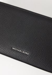 Mustmust tekstuuriga must nahast rahakott, millel on hõbedane "MICHAEL KORS" logo, peene disaini ja kvaliteetsete õmblustega.