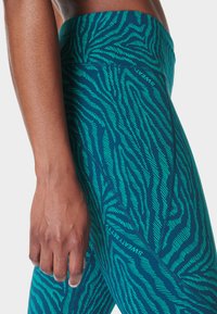 Turquoise legging met een contrasterend groen zebraprintpatroon, voorzien van een hoge taille en een gladde, flexibele stof voor actieve kleding.
