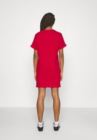 Červené bavlněné šaty v tvaru trička s krátkými rukávy, rovného střihu a kulatým výstřihem. Nosené s černými sportovními botami a bílými ponožkami.