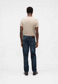 Μπεζ κοντομάνικη  μπλούζα συνδυασμένη με σκούρο μπλε τζιν παντελόνι που διαθέτει καφέ δερμάτινο έμβλημα, ορατή ραφή και κλασικό σχέδιο με πέντε τσέπες.