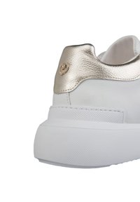 Sneaker bianco con un'applicazione in pelle oro testurizzata sul tallone e logo circolare. Presenta una punta arrotondata e una robusta suola in gomma bianca.