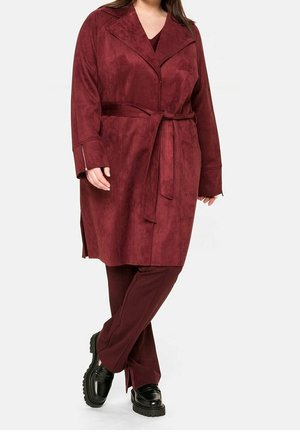 Bordeauxrode jas met suède textuur, voorzien van een ceintuur, oversized revers en zijslitten, gecombineerd met bijpassende taps toelopende broek en zwarte plateauzolen.