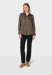 Chemise à rayures verte olive et bleu marine, avec une coupe décontractée et des manches longues. Associée à un pantalon noir et des baskets beiges.
