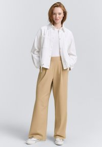 Giacca in denim bianco con due tasche frontali, abbinata a pantaloni larghi beige e sneakers bianche. Design semplice, colori neutri.