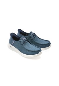Scarpe slip-on in tessuto blu con una superficie testurizzata, suola in gomma bianca e accenti in navy a contrasto. Presentano un motivo sottile e dettagli con lacci.