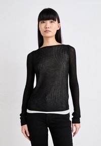 Haut en maille noir à manches longues avec un col bateau, texture transparente et un accent de bord blanc, associé à un pantalon noir.