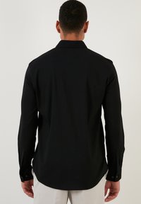 Camisa negra de manga larga con una tela texturizada, puños abotonados y dobladillo recto, que presenta un diseño de cuello clásico.