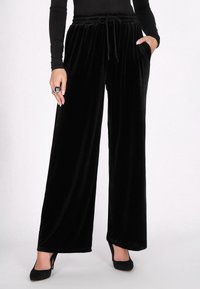 Fekete bársony széles szárú nadrág, rugalmas derékkal és húzózsinórral, oldalzsebekkel és puha, sima textúrával.