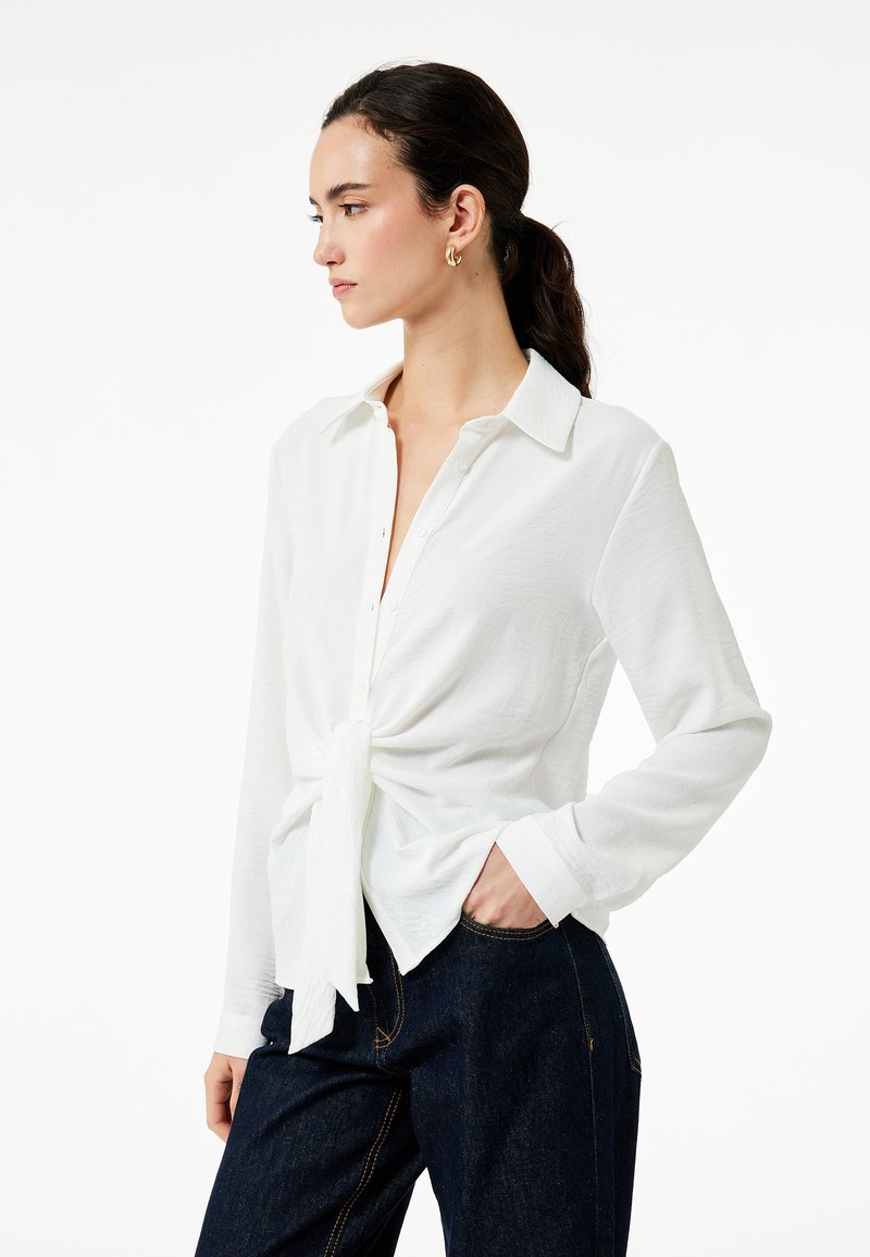 Witte overhem shirt met een geknoopte voorkant, gemaakt van textuurstof. Beschikt over een klassieke kraag en lange mouwen, gecombineerd met donkere denim.