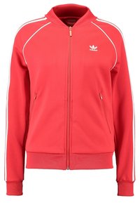 Červená bunda na zip z texturované látky. Má bílé boční pruhy a žebrovaný lem a manžety. Obsahuje dvě kapsy na zip.