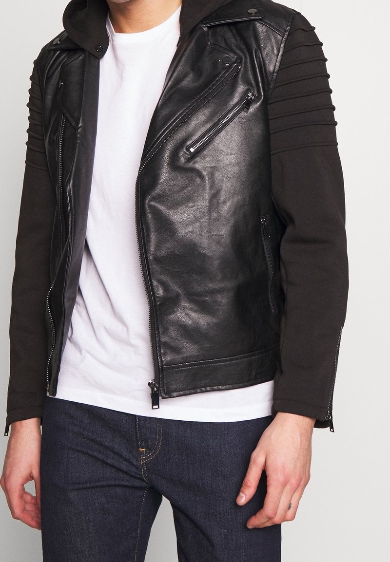 Giacca da motociclista nera in pelle con maniche in tessuto a coste, zip argento e cappuccio staccabile. Presenta una vestibilità slim e un design minimalista.