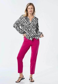 Zebraprint blouse met lange mouwen in zwart-wit, gecombineerd met strakke roze broek en zwarte slippers, met een decoratieve hardware-accent.