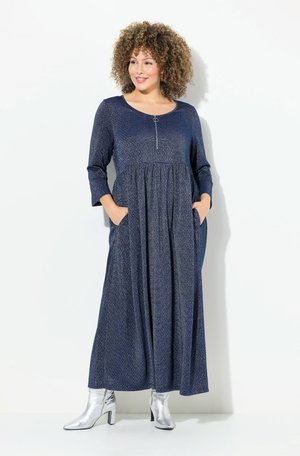 Langes, marineblaues Kleid mit strukturiertem Muster, Rundhalsausschnitt, Dreiviertelärmeln und Taschen; mit einem Reißverschluss auf der Vorderseite. Silberne Knöchelstiefel.