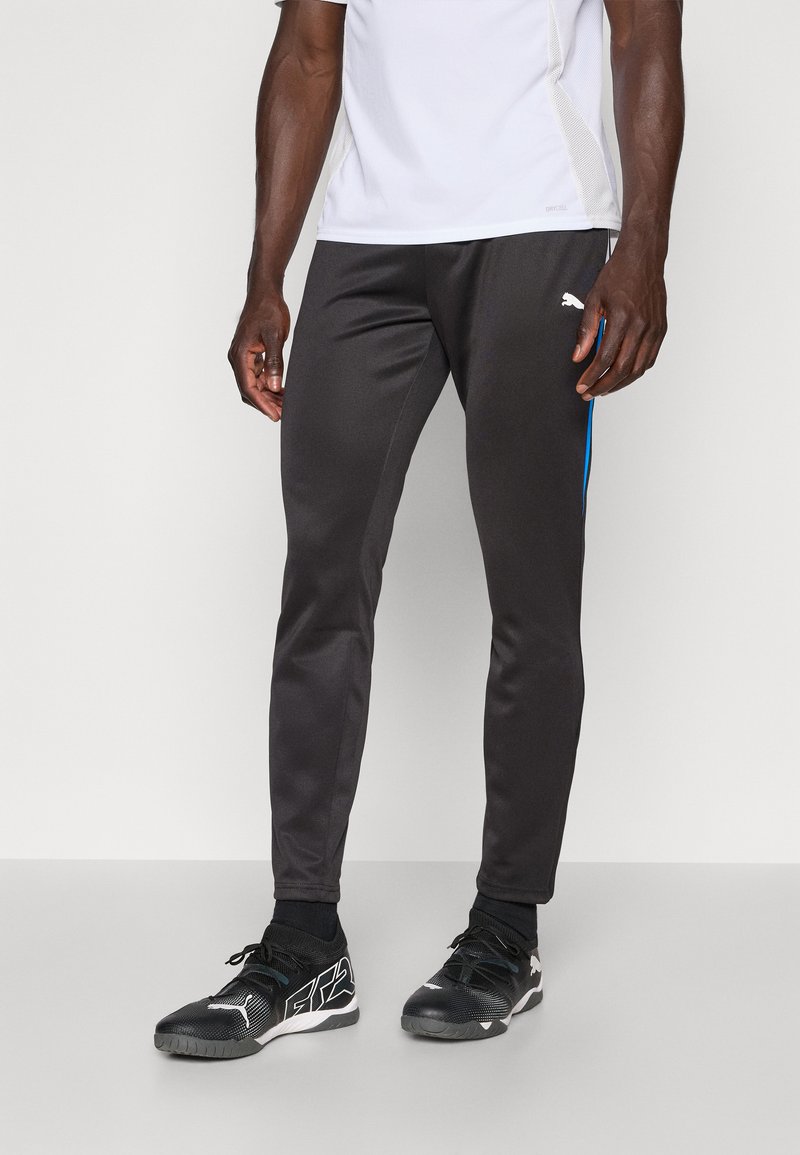 Pantaloni sportivi negri cu o croială slim, având dungi laterale albastre și un logo alb în partea superioară a coapsei, confecționați dintr-un material neted și elastic.
