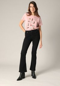 T-shirt en coton rose avec des motifs graphiques, associé à un jean noir évasé taille haute et des bottines noires à talons.