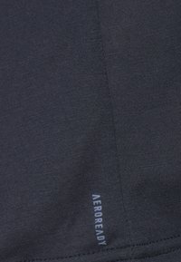 Camisa deportiva de color azul marino oscuro con una textura suave; presenta una pequeña etiqueta "AEROREADY" cerca del dobladillo. Diseñada para la comodidad y el rendimiento.