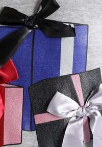Tre scatole regalo di vari colori: una scatola blu con un nastro nero, una scatola rosa con un nastro rosso e una scatola nera con un nastro argento. Tutte presentano superfici luccicanti.