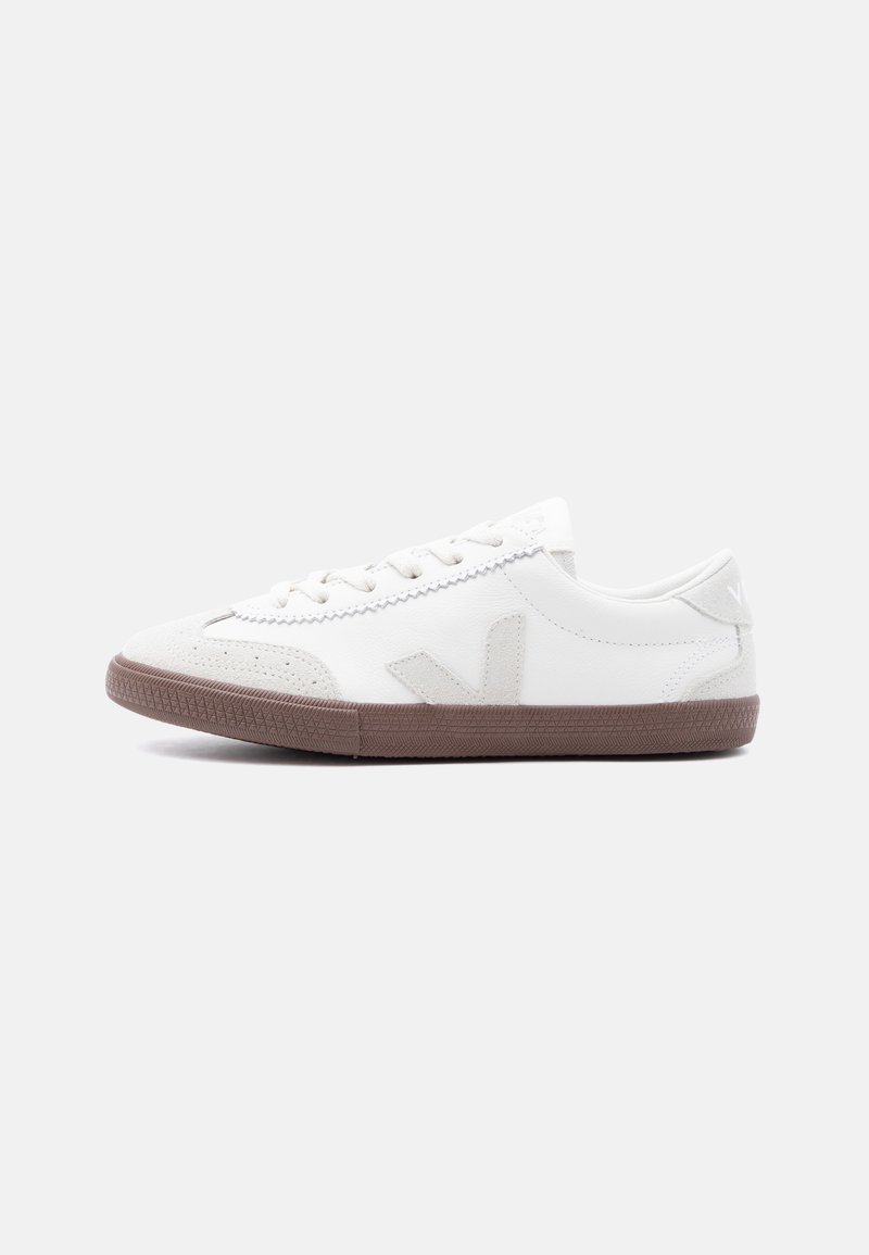 Λευκό χαμηλό αθλητικό παπούτσι με μπεζ τζίν suede λεπτομέρειες, καφέ λαστιχένια σόλα και σχέδιο με κορδόνια σε απλό ανοιχτό γκρι φόντο.