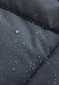 Tissu noir matelassé avec des gouttes d'eau à la surface, mettant en valeur une texture lisse et un motif côtelé provenant de la couture.