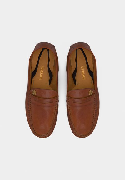 Paire de mocassins Versace en cuir marron, avec bouts arrondis, coutures mocassin et détail de bouton Medusa doré sur fond blanc.