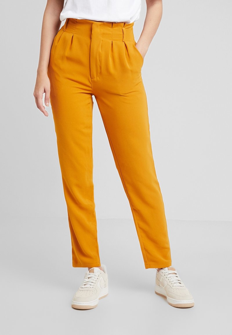 Klart orange högmidjade byxor med veck, med en figursydd silhuett och sidofickor, kombinerat med krämfärgade sneakers.