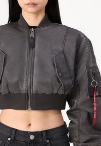 Cropped bomber jacket in gray with a textured finish, ribbed cuffs, and zippers. Includes two front pockets and a red tag saying "REMOVE BEFORE FLIGHT."