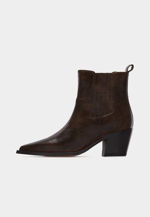 Tamno smeđa kožna gležnjača s špicastim vrhom, blok petom i trakicom za povlačenje na stražnjoj strani, prikazana u profilu na bijeloj pozadini.