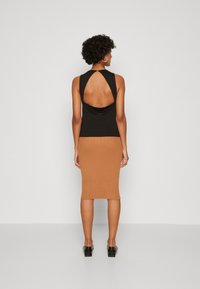 Schwarzes ärmelloses Top mit offenem Rücken, kombiniert mit einem gerippten, beigen Bleistiftrock. Das Outfit zeichnet sich durch eine figurbetonte Silhouette und eine glatte Textur aus.