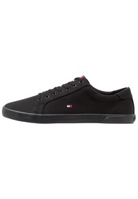 Schwarze Canvas-Sneaker mit niedrigem Design, runder Zehenpartie, schwarzer Gummisohle und kleinem Emblem in rot, weiß und blau.