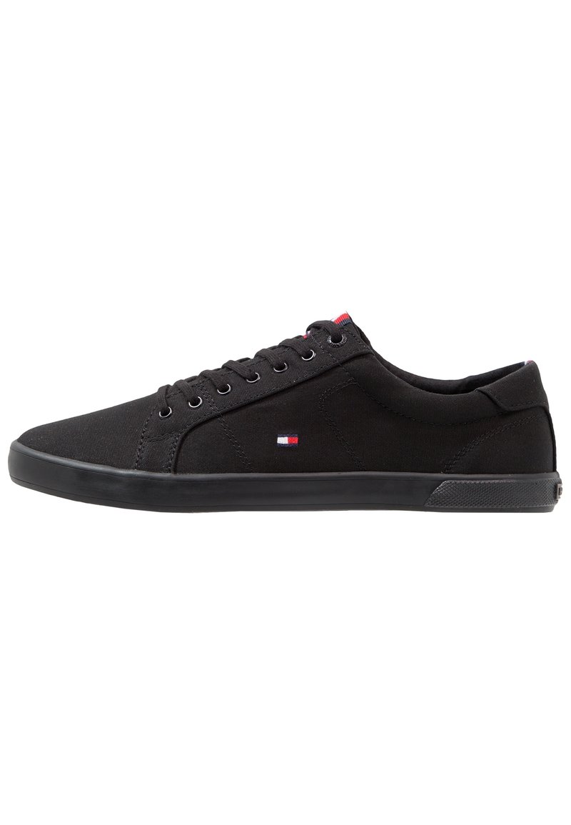 Schwarze Canvas-Sneaker mit niedrigem Design, runder Zehenpartie, schwarzer Gummisohle und kleinem Emblem in rot, weiß und blau.