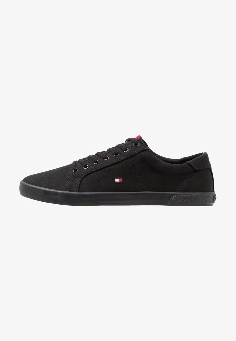 Schwarze Canvas-Sneaker mit niedrigem Design, runder Zehenpartie, schwarzer Gummisohle und kleinem Emblem in rot, weiß und blau.
