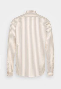 Světle béžová dlouhá košile s bílými vertikálními pruhy, s límečkem, zakončená knoflíkovými manžetami a zakulaceným lemem. Bavlněná tkanina, volný střih.