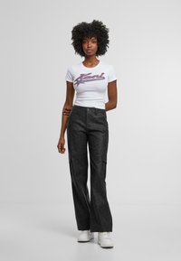 Camiseta blanca con texto gráfico en azul y rojo combinada con pantalones cargo negros de cintura alta que tienen bolsillos laterales y un ajuste relajado.